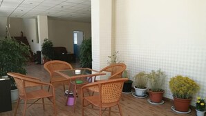 A room with a wooden floor, a glass table, and wicker chairs. There are potted plants along the wall.