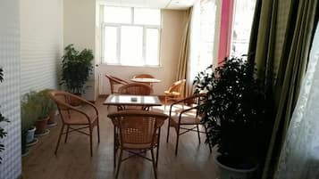 Un comedor con una mesa y sillas, plantas en macetas y un ventanal con cortinas.
