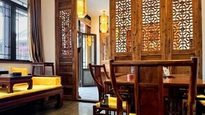 Un interior tradicional de madera con una mesa de comedor y sillas, un sofá con cojines amarillos y paneles de madera decorativos.