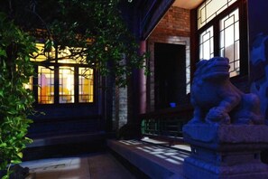 Una entrada de edificio con una estatua de león de piedra, fachada de ladrillo e iluminación cálida en el interior.