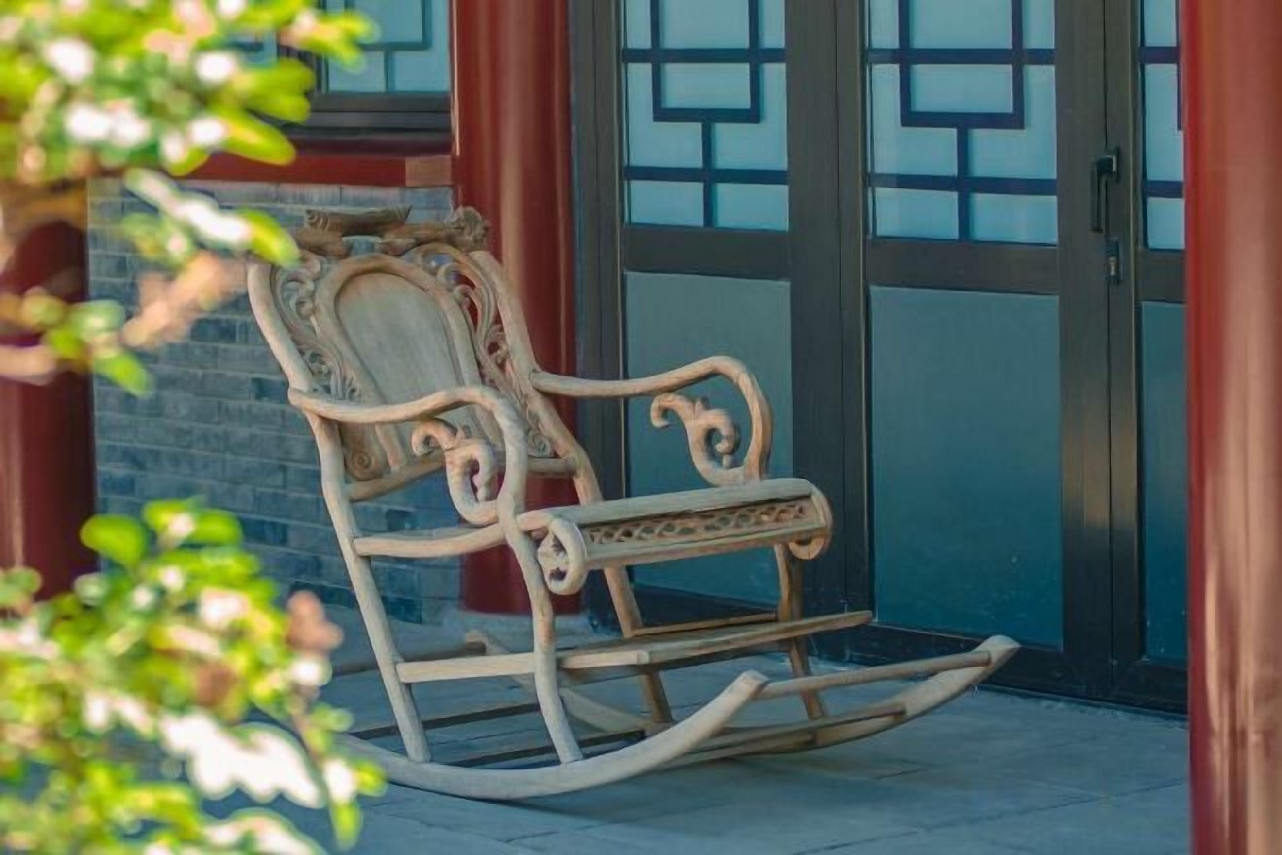 A rocking chair outside a building with a glass door and a brick wall.
