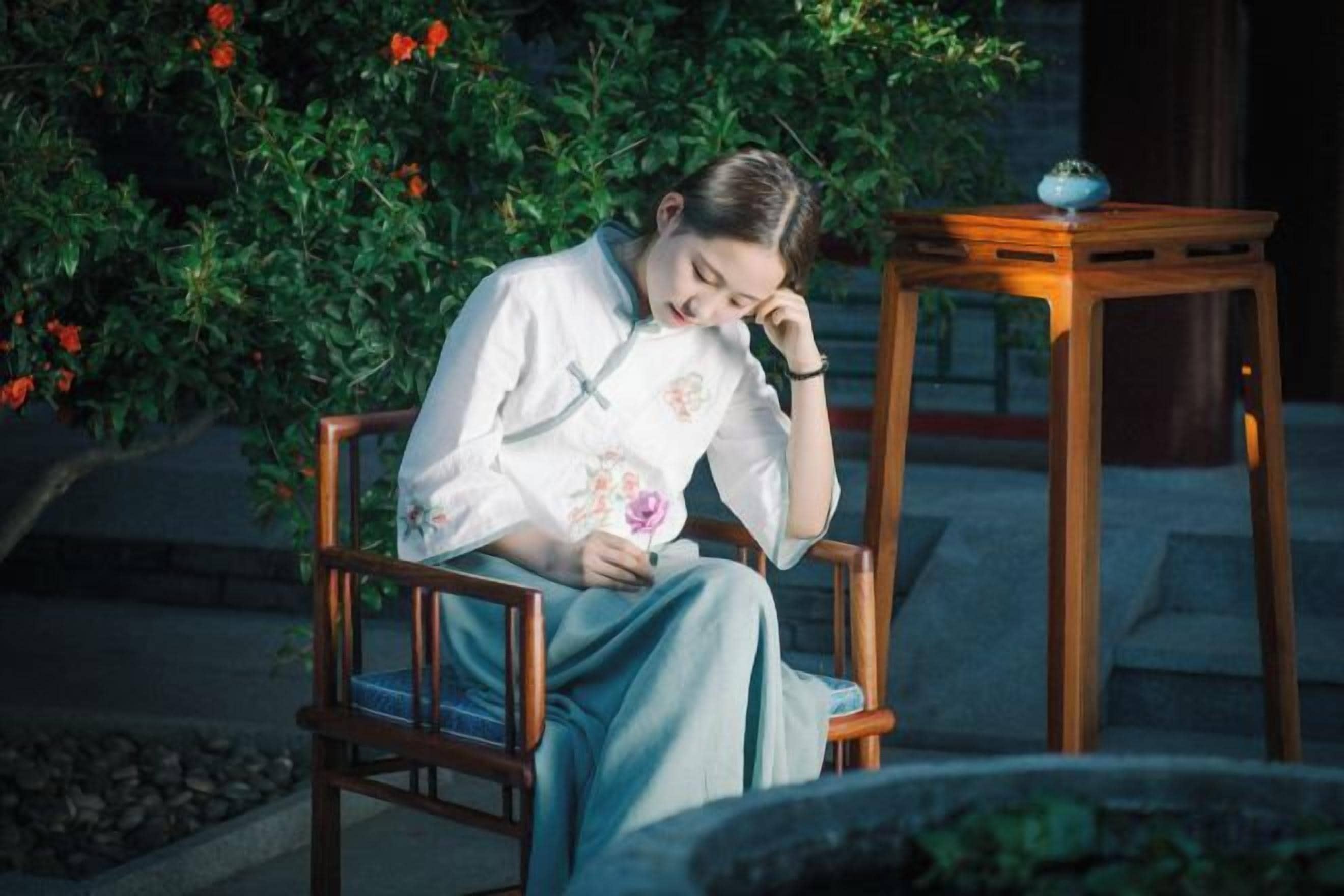 Una persona seduta su una sedia di legno all'aperto, con un tavolo nelle vicinanze.