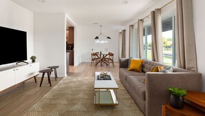 Una sala de estar moderna con sofá, mesa de centro, televisor y comedor.
