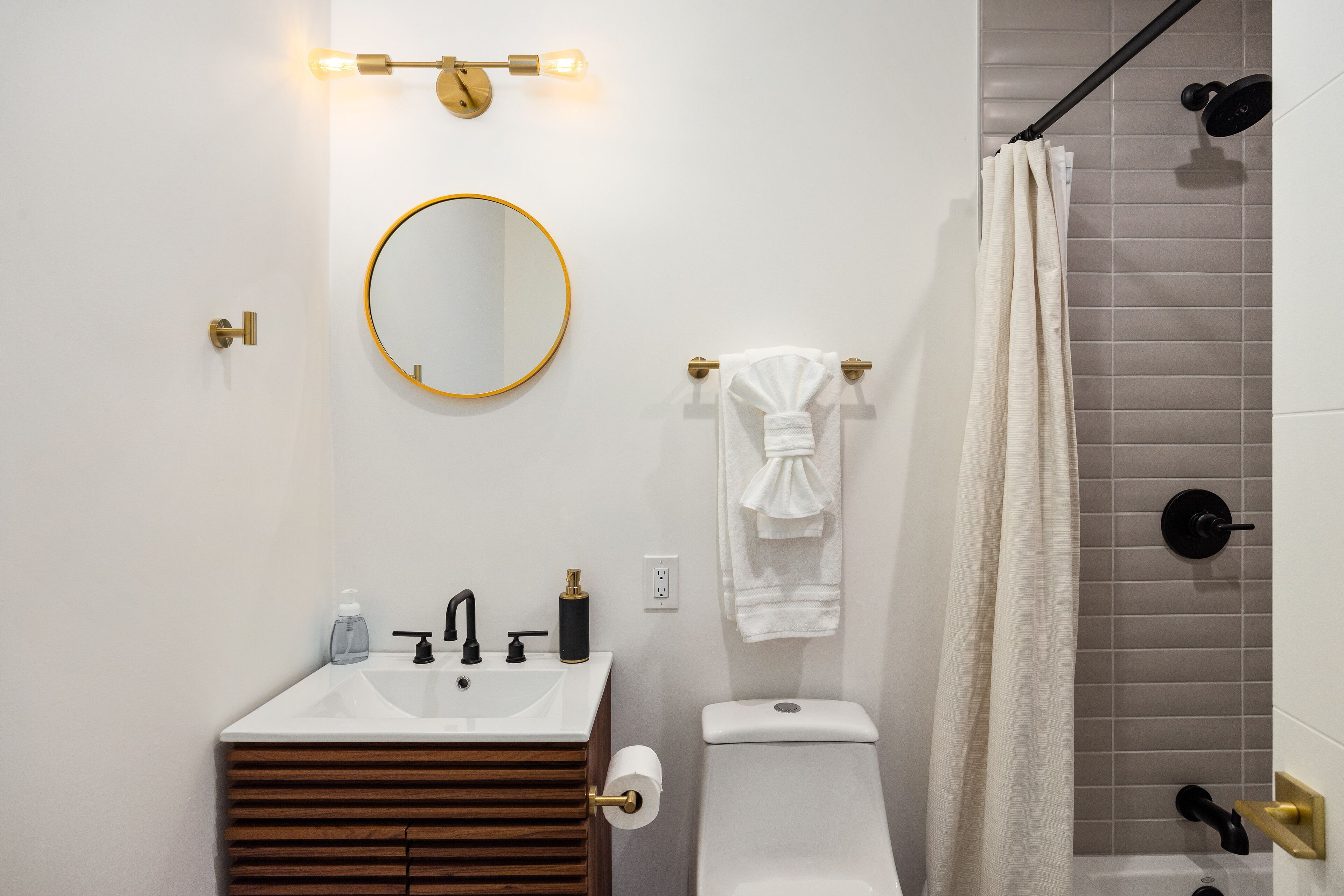 Et moderne badeværelse med vask, spejl, toilet og bruseforhæng.
