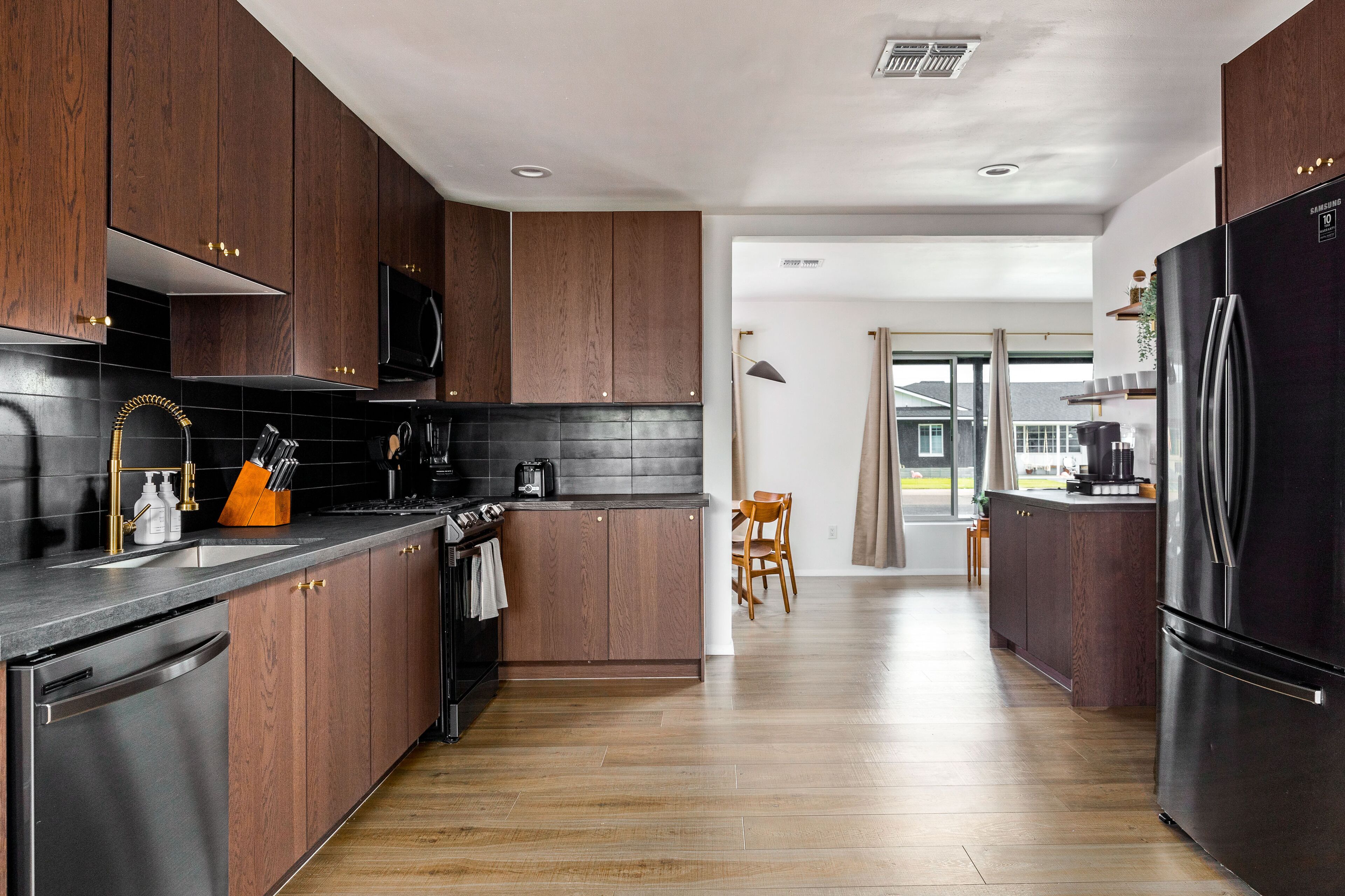 Een moderne keuken met donkere houten kastjes, een zwarte koelkast en een eethoek met een houten tafel.