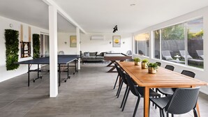Una habitación amplia con una larga mesa de madera y sillas, una mesa de ping pong y un sofá.