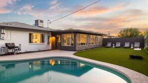 Una casa moderna con piscina, un patio con sillas de descanso y un césped cuidado.