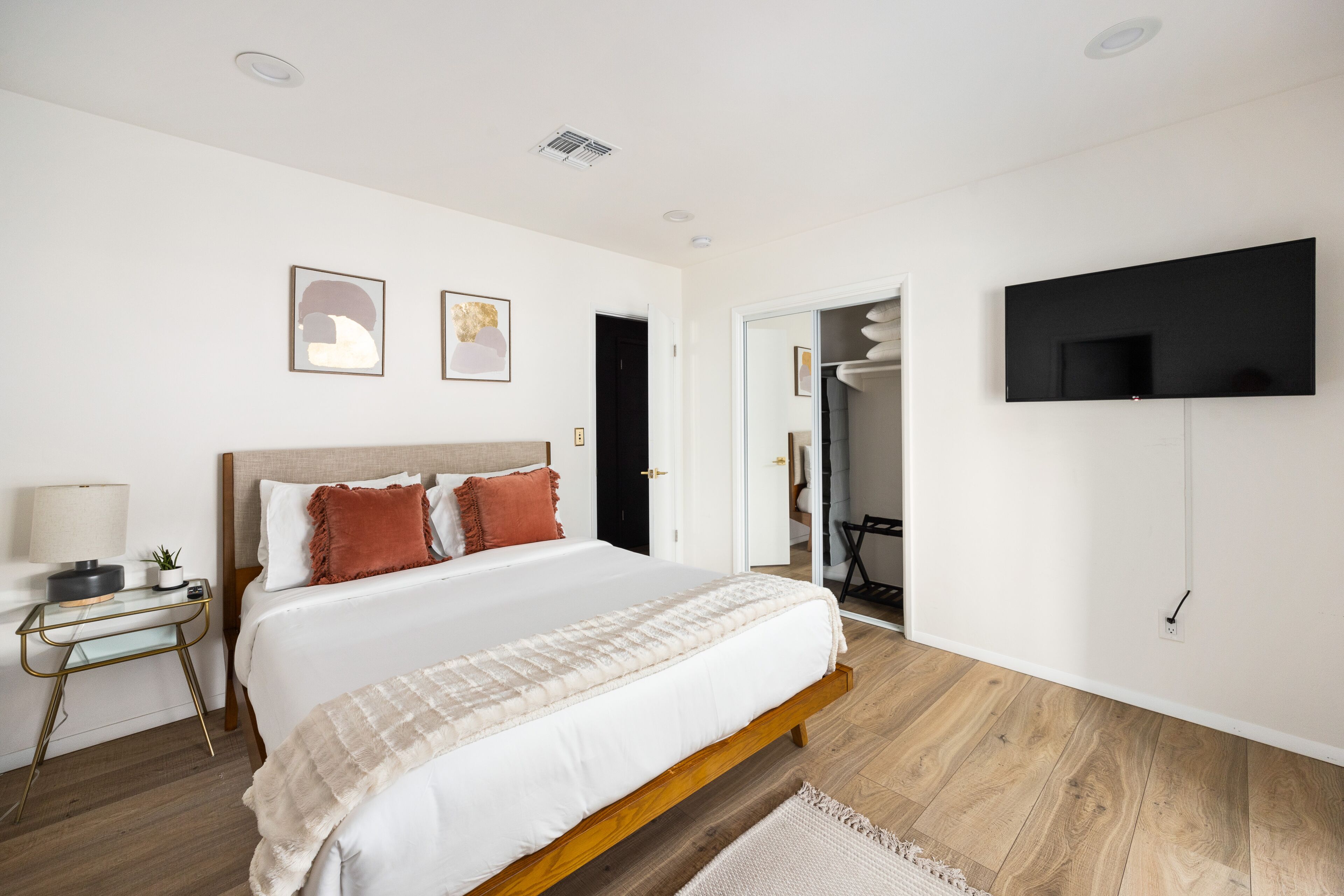 A modern bedroom with a large bed, bedside table, and a flat-screen TV mounted on the wall.