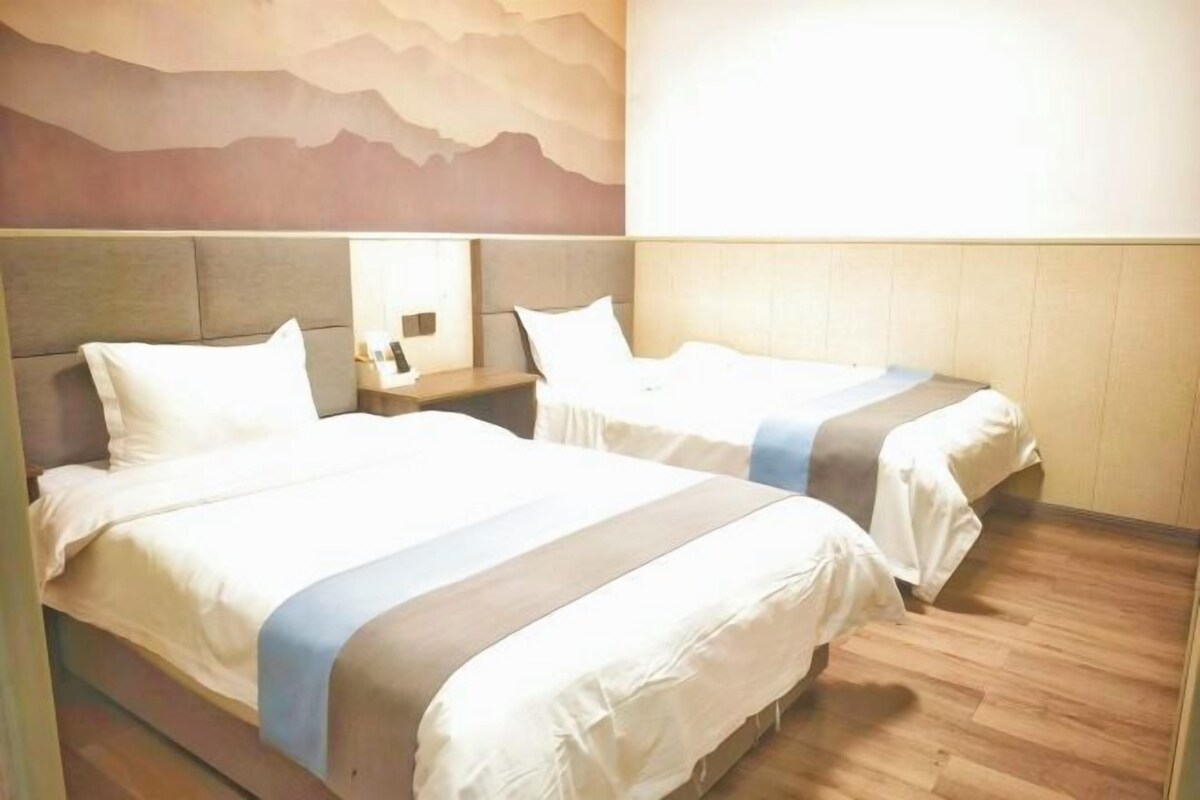 A hotel room with two beds, a nightstand, and a wall-mounted lamp.