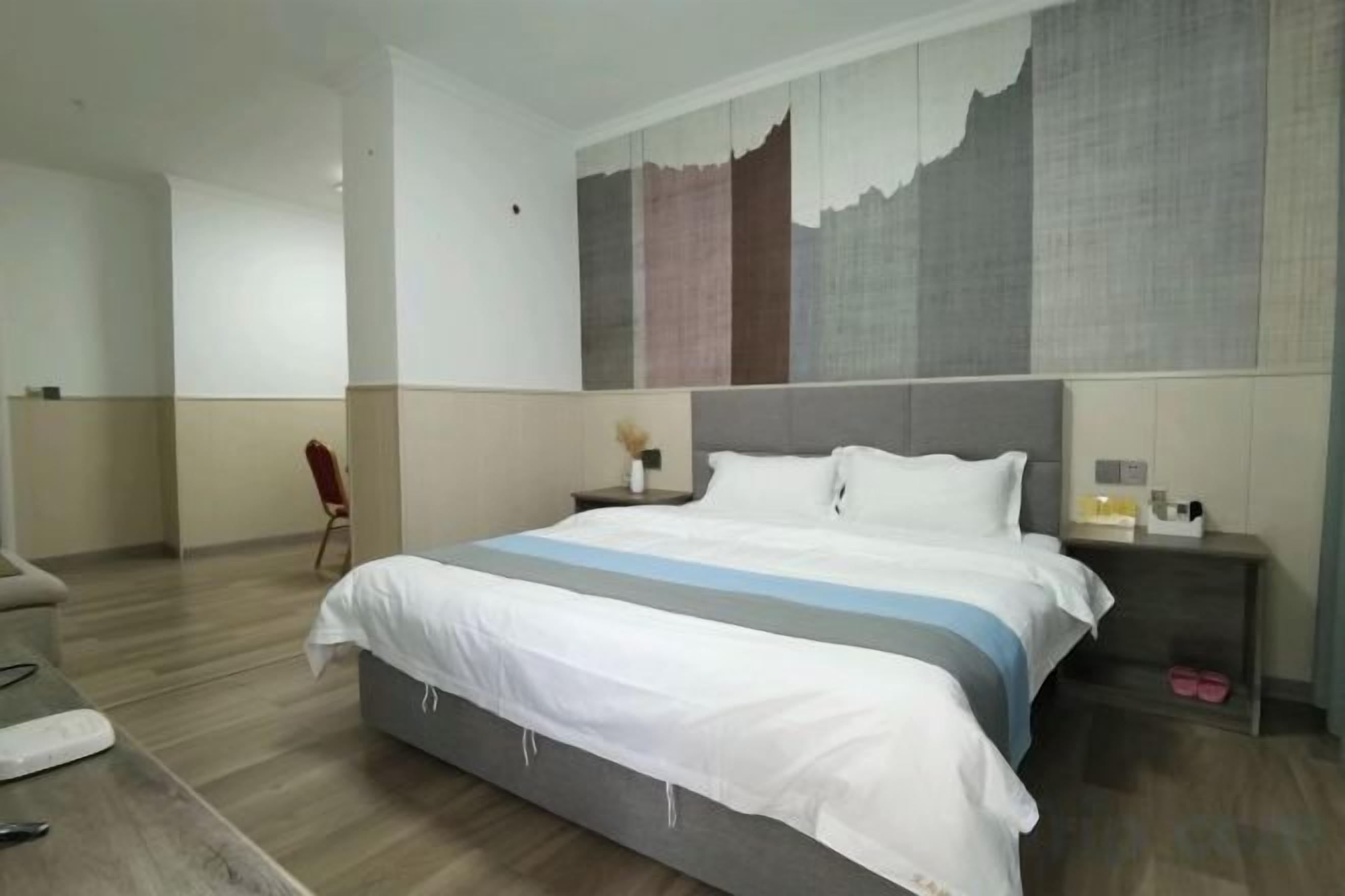 A hotel room with a large bed, a nightstand, a chair, and a painting on the wall.