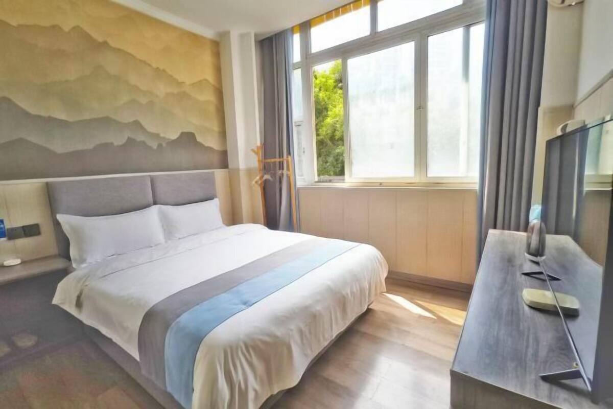 A hotel room with a large bed, a desk, and a window with curtains.