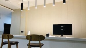 A reception desk with two wooden chairs, a flat-screen monitor, and pendant lighting. - Aishang City Inn (Chongqing)