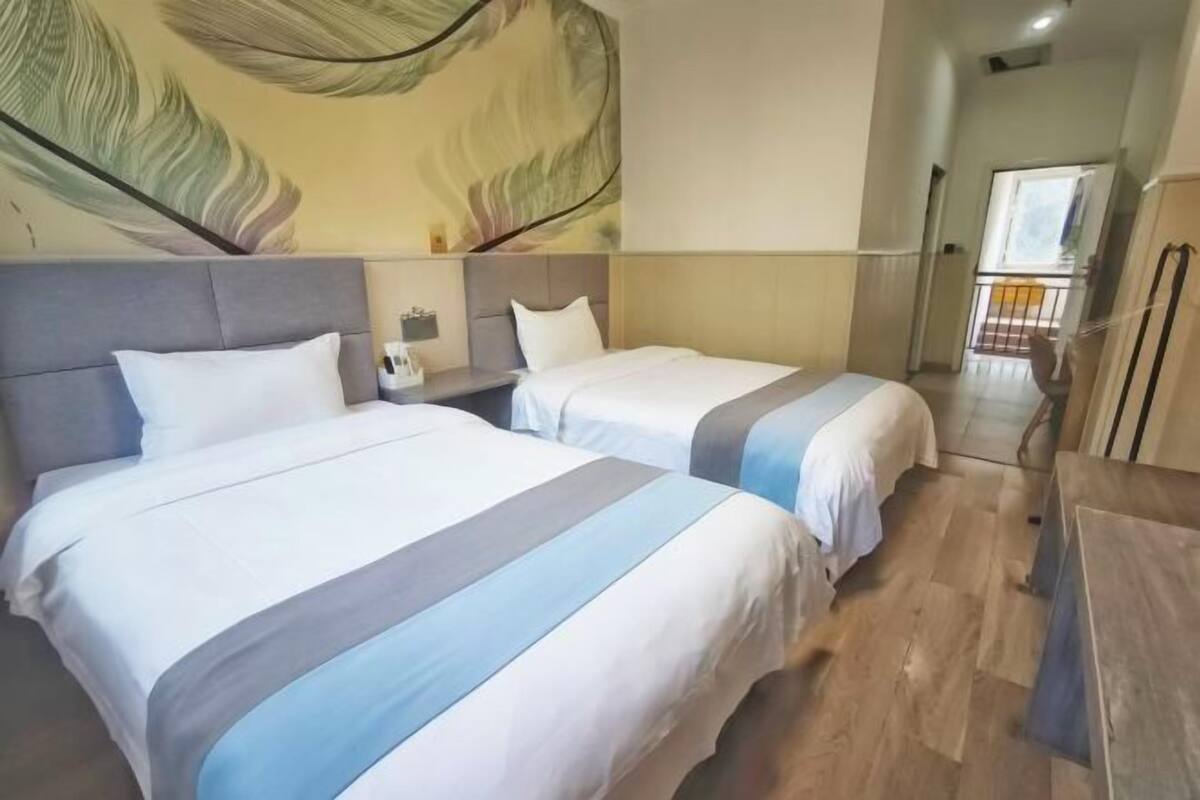 A hotel room with two beds, a large wall mural, a small table, and a balcony view.