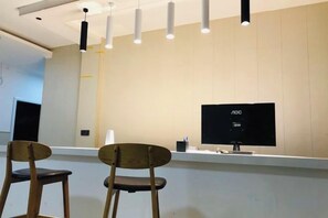 Aula, jossa on litteänäyttöinen monitori, kaksi puista tuolia ja riippuvalaisimet.