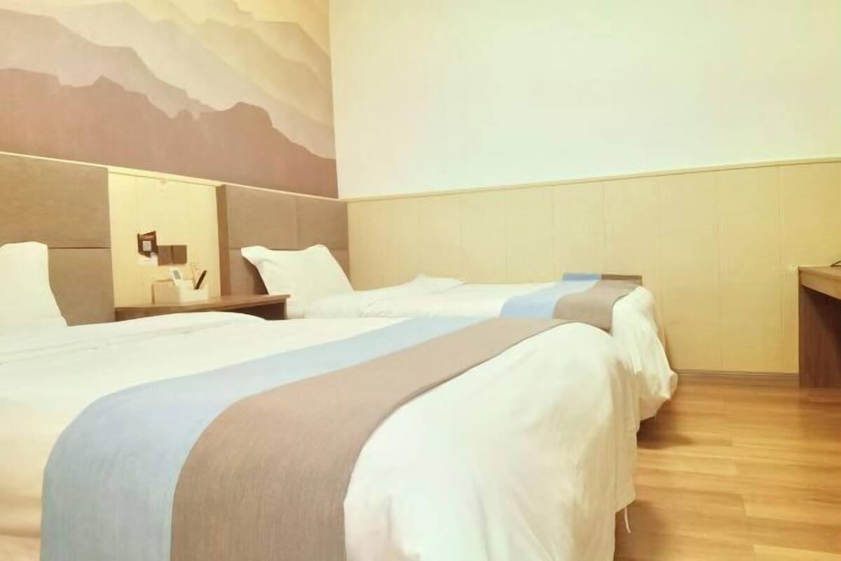 A hotel room with two beds, a wooden floor, a wall-mounted mirror, and a mountain mural.