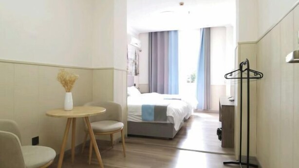 A hotel room with a bed, a small round table with a vase, a chair, and a coat rack. - Aishang City Inn (Chongqing)