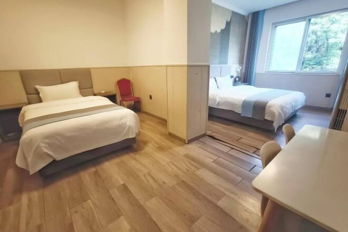 A hotel room with a large bed, a small table, and a window with a view of trees.