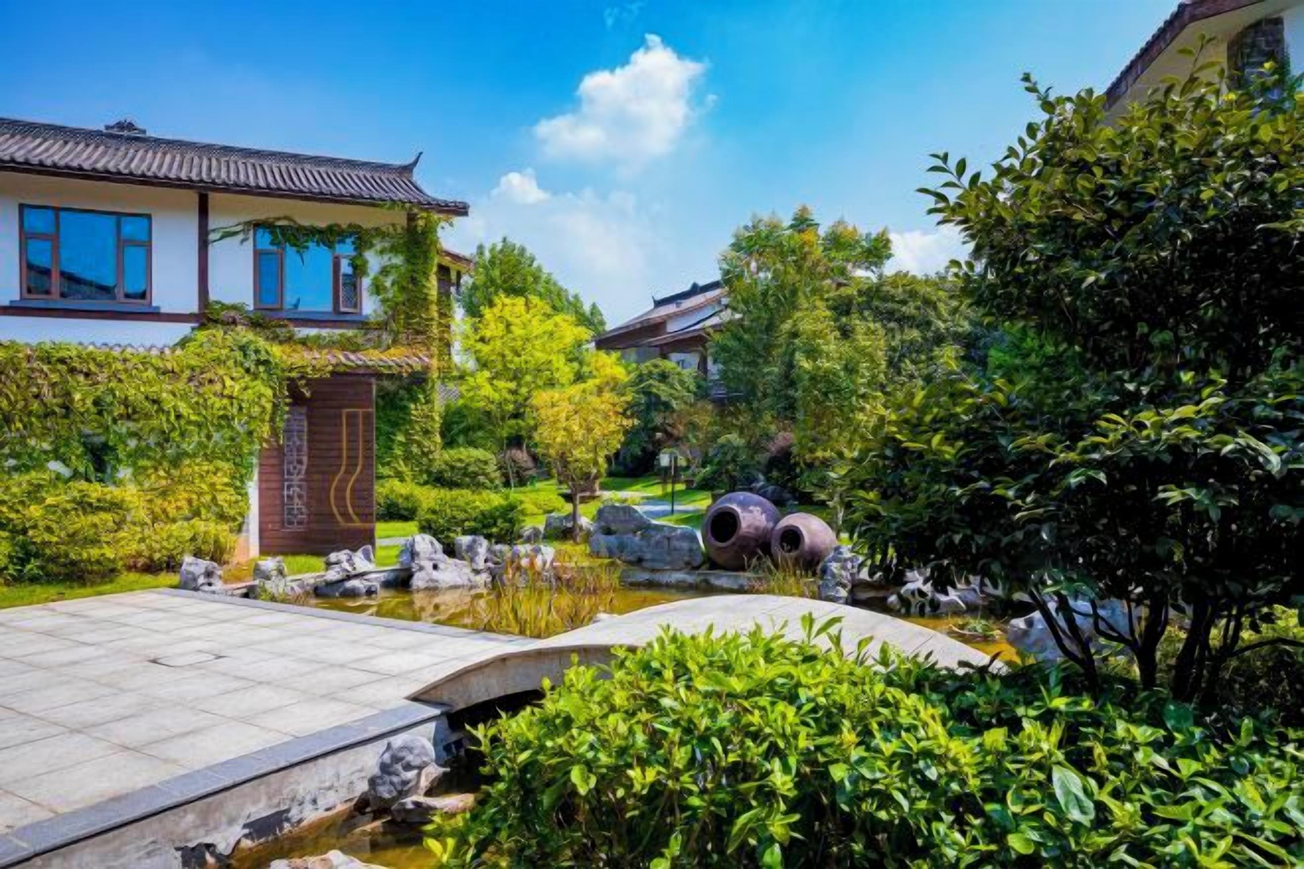 A traditional-style building with a garden, including a pond, rocks, and trees.