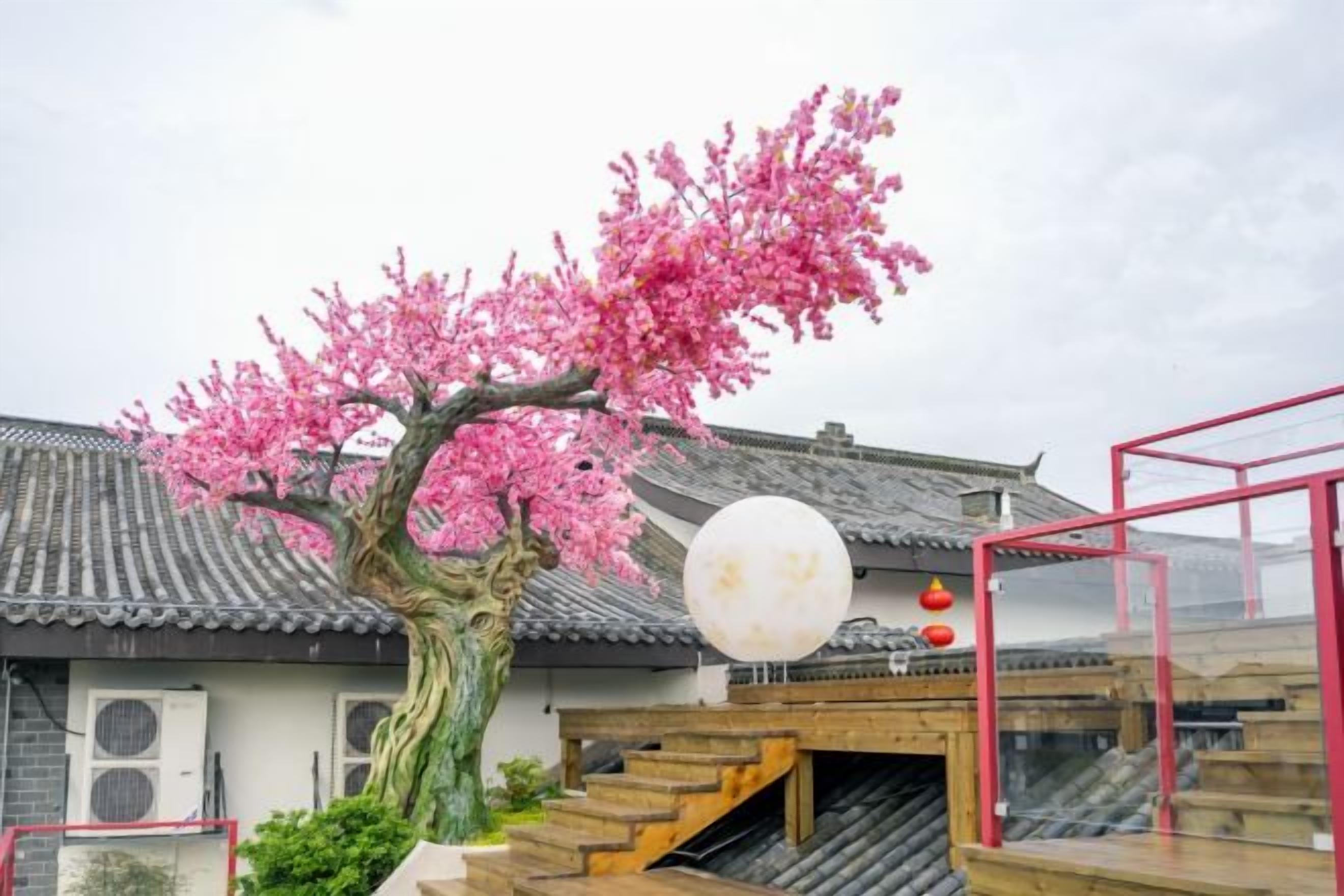 Un edificio tradicional con un cerezo en flor, escaleras de madera y un farol rojo.