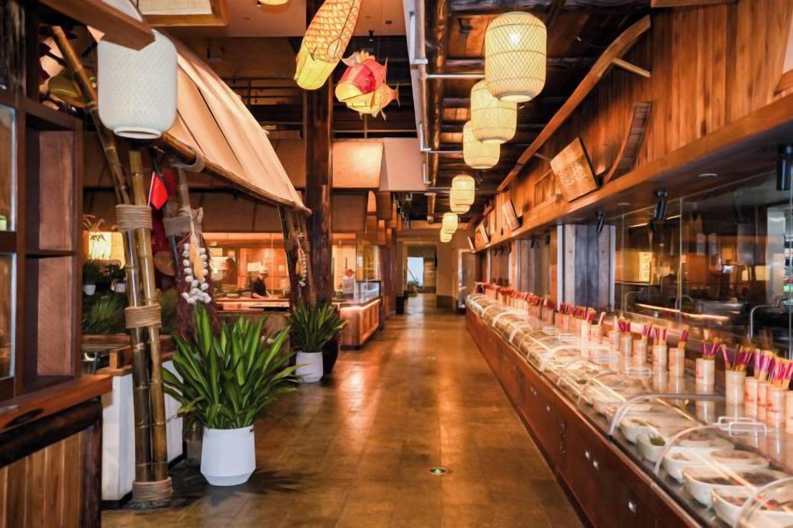 A restaurant interior with wooden beams, hanging lanterns, and a long counter with food items.