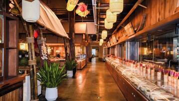 A restaurant interior with wooden beams, hanging lanterns, and a long counter with food items.
