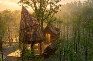 A wooden cabin with a conical roof, surrounded by trees.