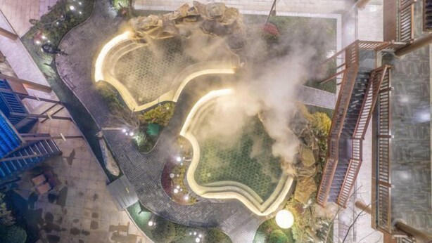 Un área de aguas termales con una piscina central, rodeada de barandas de madera y vegetación.