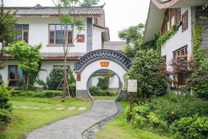 A traditional building with a tiled roof, a stone pathway leading to an archway, and lush greenery. - Yangshan Lake Yuyao Inn (Xiangyin)