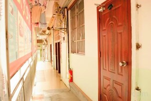 A narrow corridor with a red door, a fire extinguisher, and a window with bars.