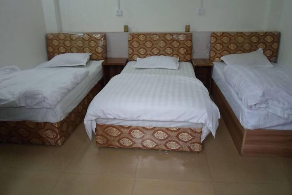 Una habitación con tres camas individuales, cada una con cabecero estampado y ropa de cama blanca.