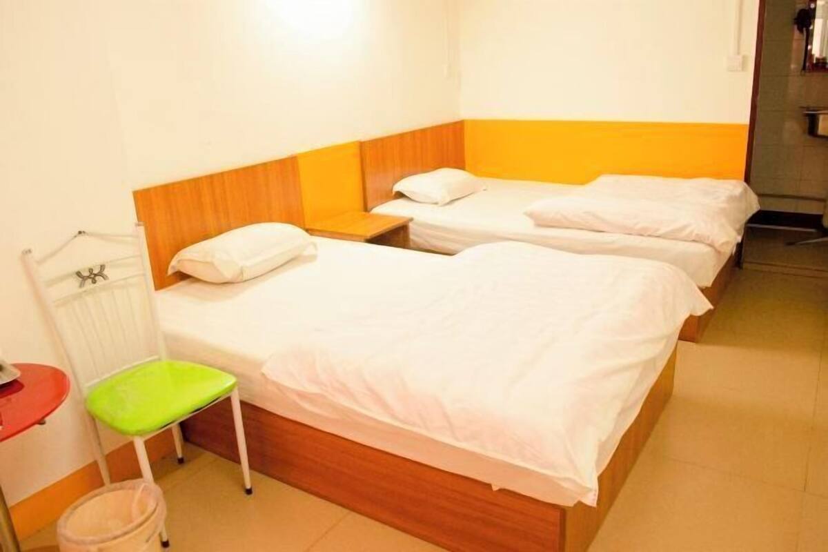 Habitación de hotel con dos camas individuales, una mesita, una silla y un radiador.