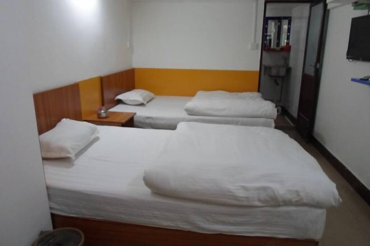 Habitación de hotel con dos camas individuales, un cabecero de madera, una mesita con lámpara y un espejo en la pared.