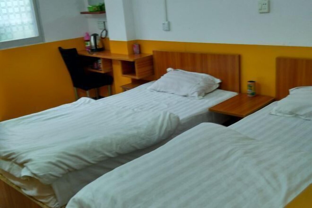 A room with two single beds, a wooden nightstand, a chair, and a shelf with personal items.
