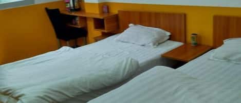 A room with two single beds, a wooden nightstand, a chair, and a shelf with personal items.