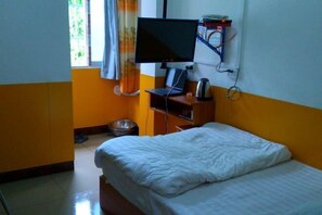 Een hotelkamer met een bed, een bureau met een computer, een televisie en een raam met gordijnen.
