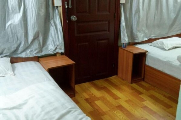 A room with two single beds, a wooden door, and a small wooden nightstand.