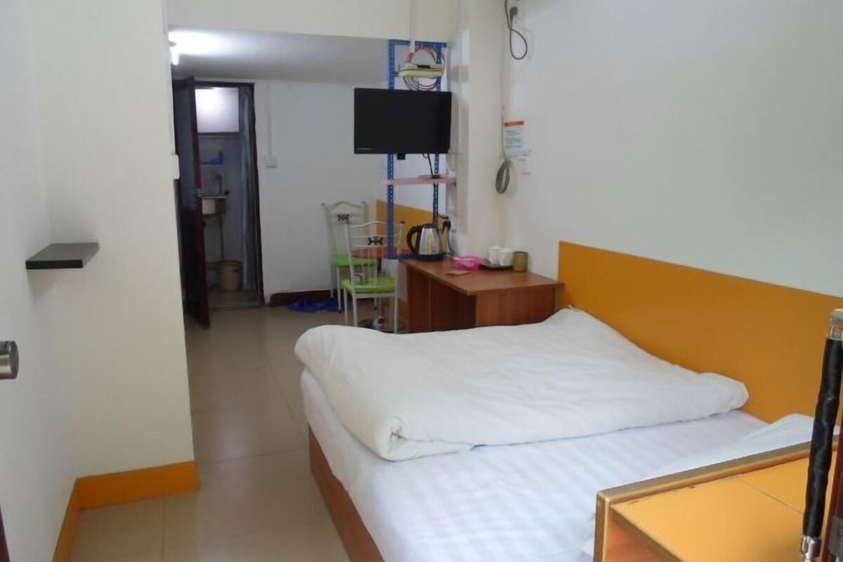 A hotel room with a bed, a desk, a chair, a television, and a small bathroom visible in the background.