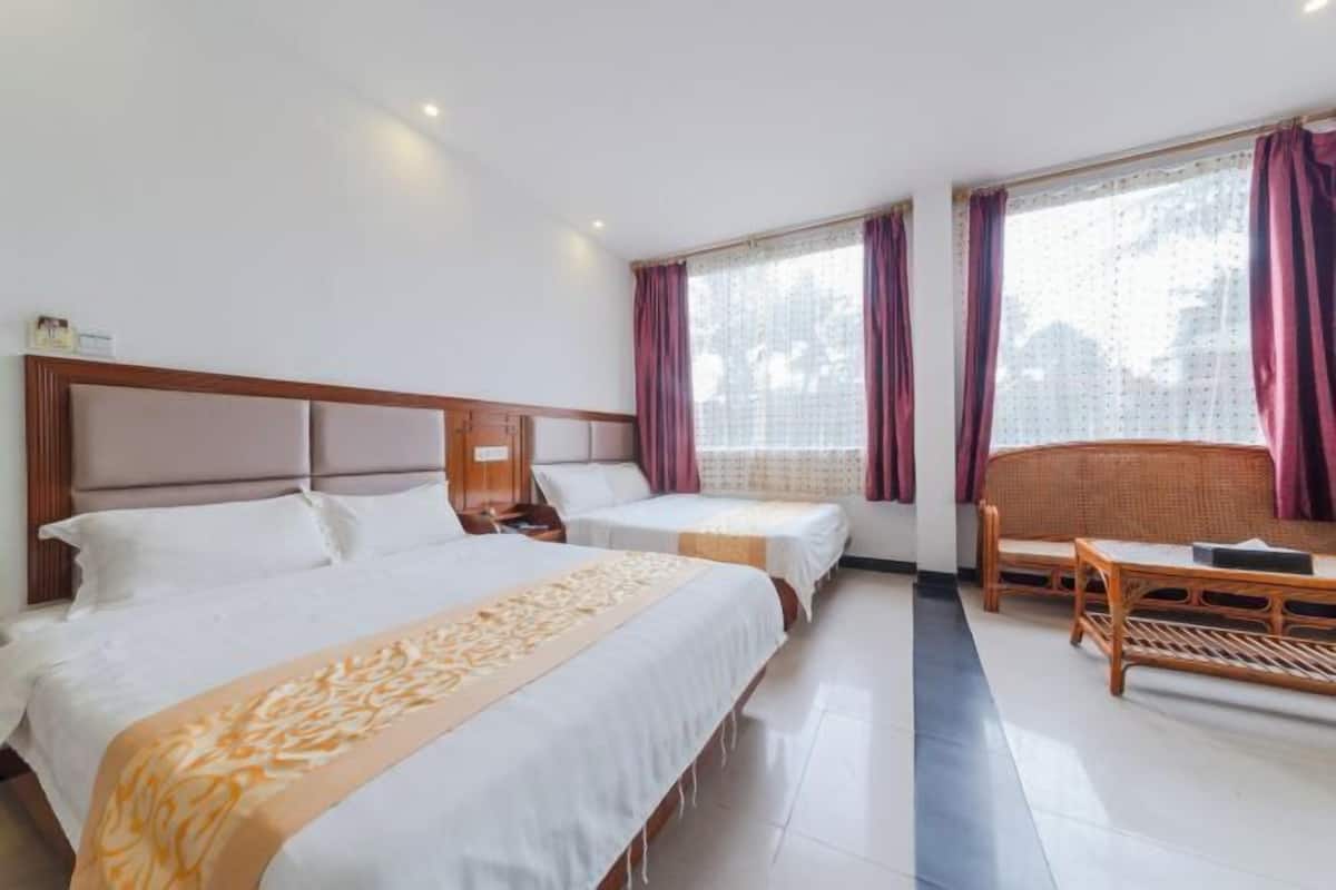 A hotel room with two beds, a wooden headboard, a nightstand, a wicker sofa, and a window with curtains.