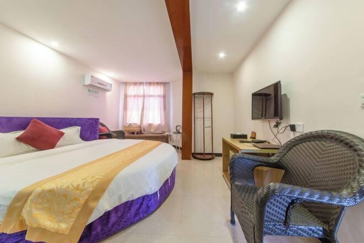 A hotel room with a large bed, a desk, a chair, and a television on the wall.