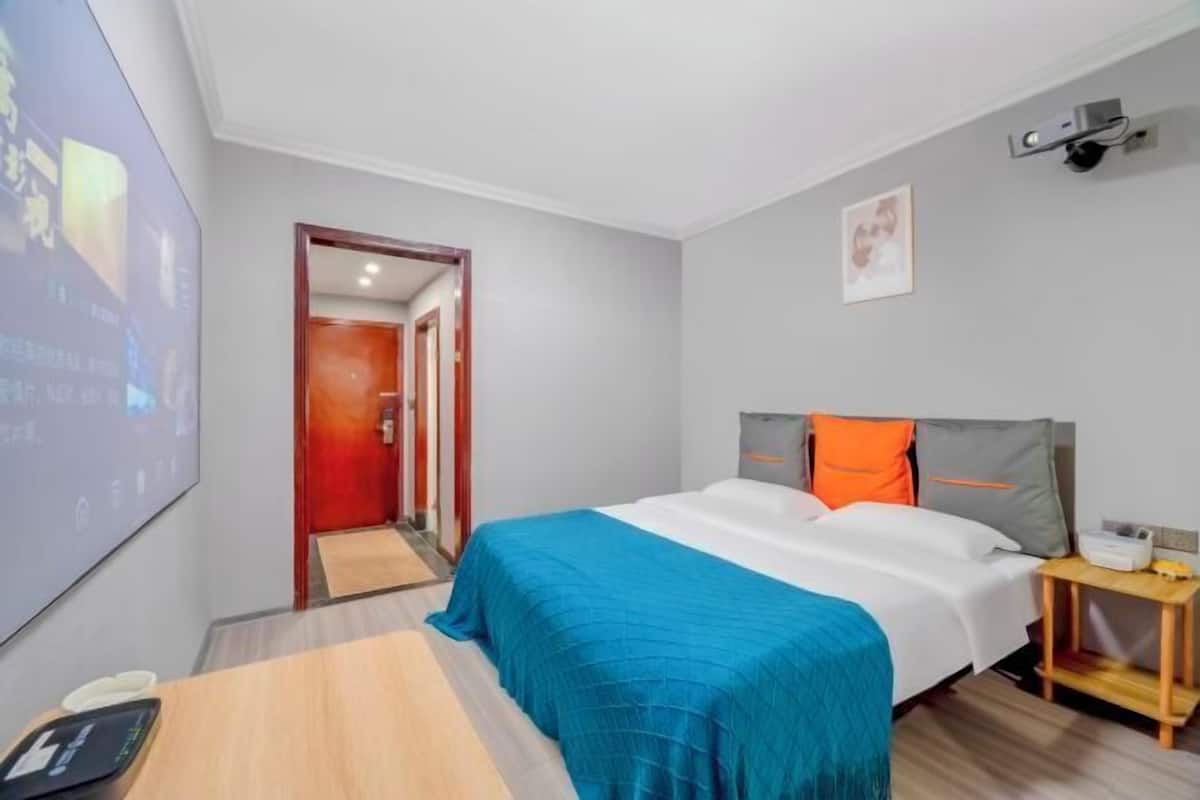 Une chambre d’hôtel équipée d’un lit, d’un bureau, d’une chaise, d’une table de chevet et d’un projecteur fixé au mur.