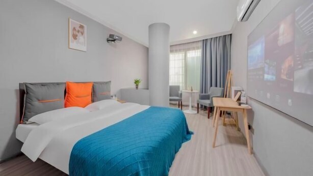 A hotel room with a bed, a desk, a chair, a small table, a plant, and a wall-mounted TV. - Muxi City Hotel (Hengyang Jiefang Road) (Hengyang)