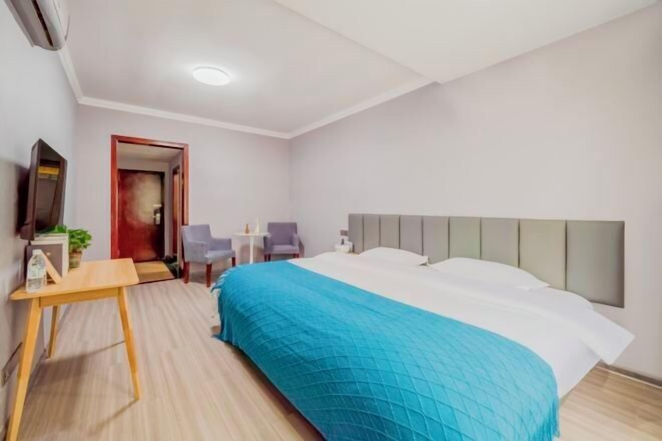 A hotel room with a bed, a desk, a chair, a TV, and a door.