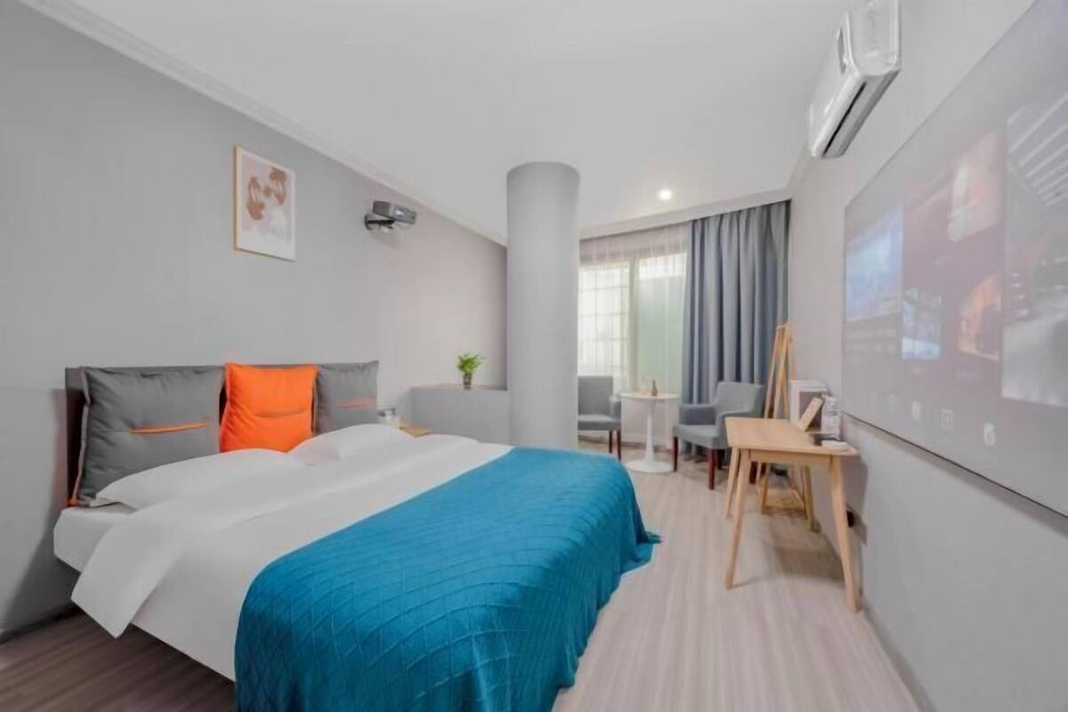 Une chambre d’hôtel équipée d’un lit, d’un bureau, d’une chaise, d’une petite table et d’un téléviseur fixé au mur.