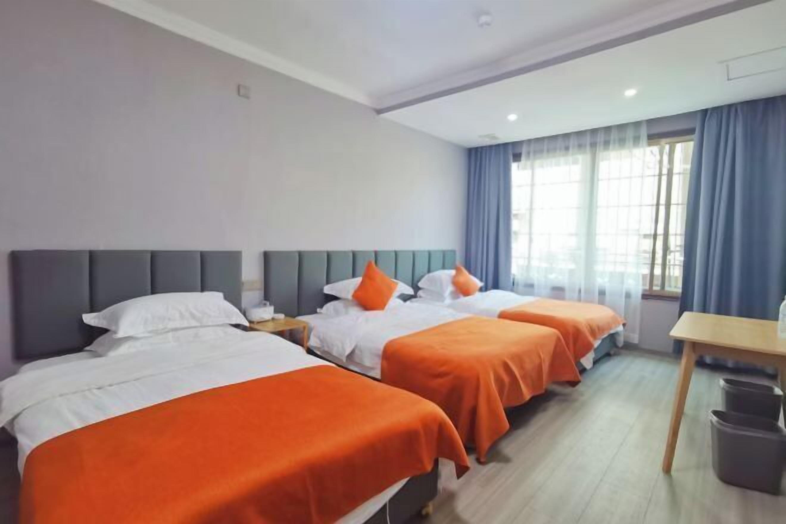 Een hotelkamer met drie bedden, een houten bureau en een prullenbak.