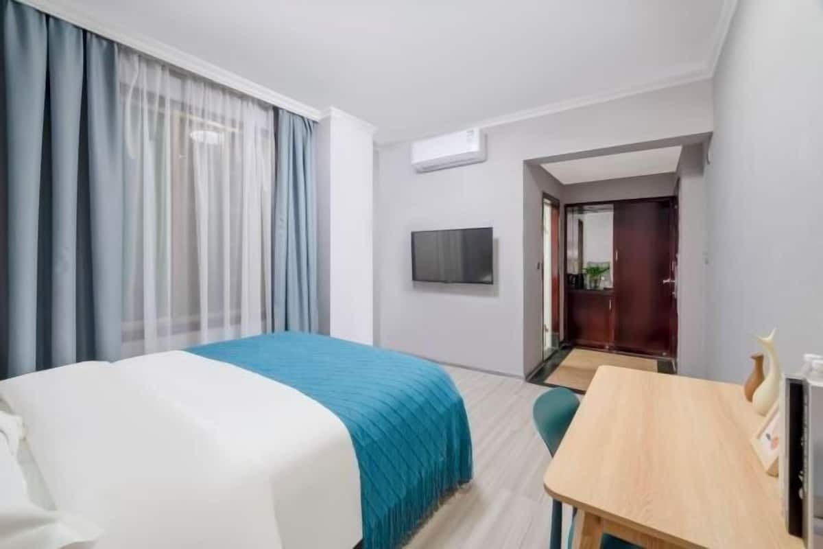 Une chambre d’hôtel équipée d’un lit, d’un bureau, d’une télévision et d’une porte donnant accès à une salle de bain.
