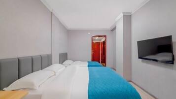 A modern hotel room with a bed, a TV mounted on the wall, and a red door in the background.