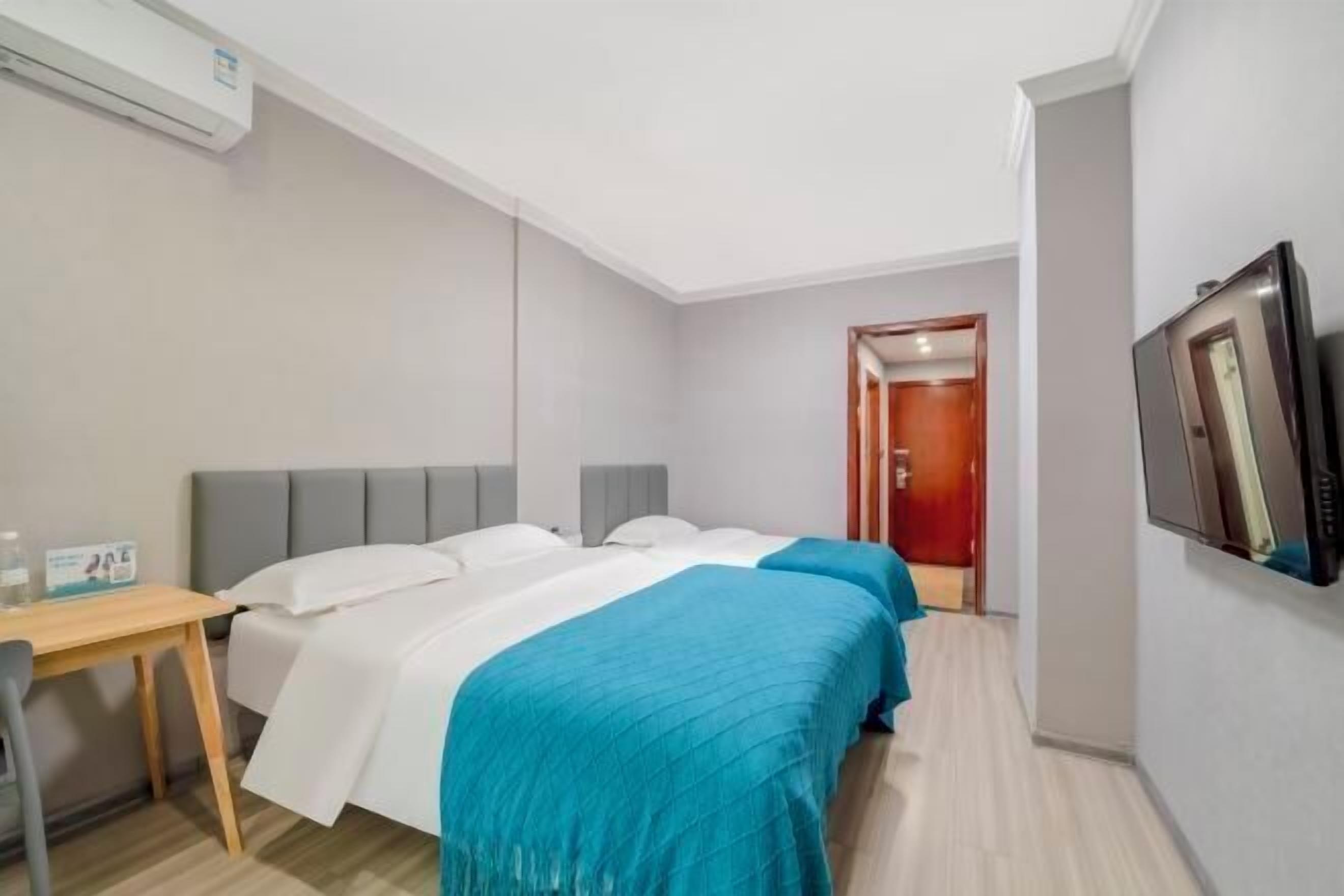 Quarto de hotel com duas camas, uma mesa, televisão e ar condicionado.