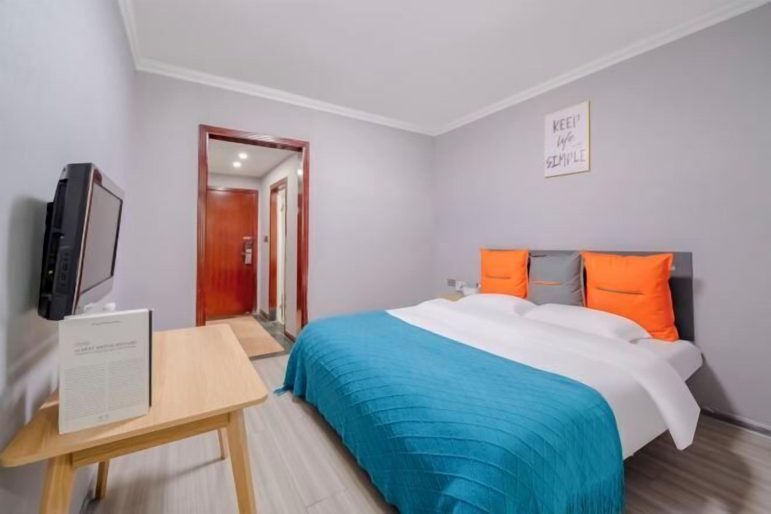 Una habitación de hotel con cama, televisor, una mesita y una puerta que da a otra habitación.