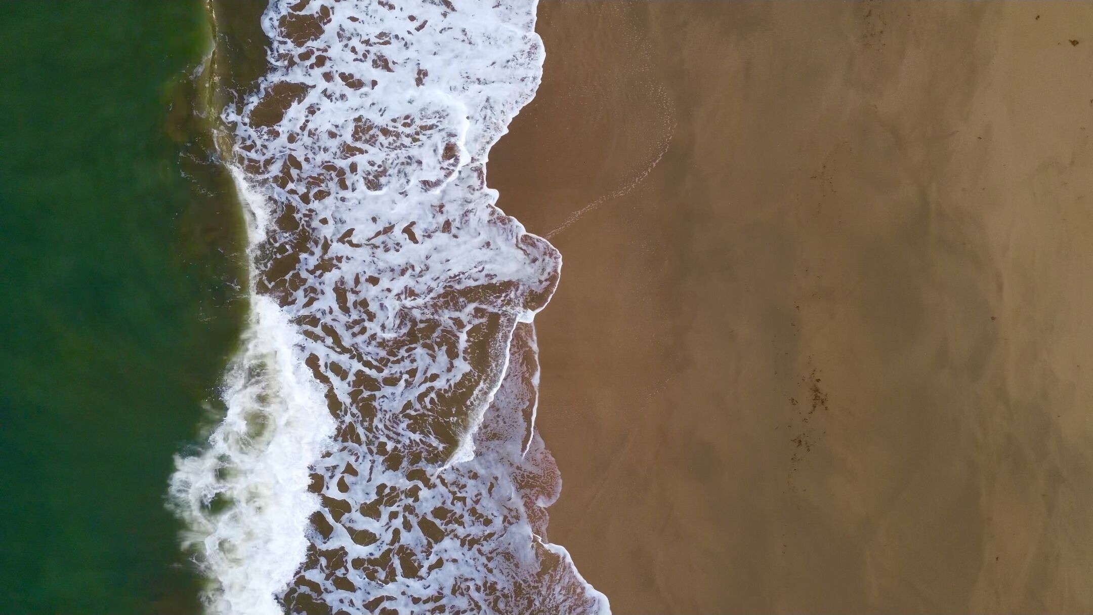 An aerial view of a beach with waves crashing onto the shore.
