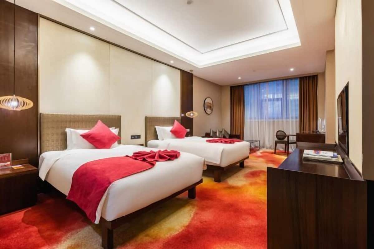 A hotel room with two beds, a desk, and a TV.